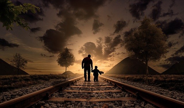 the silhouette of an older man and a young boy walking toward the horizon on a train track