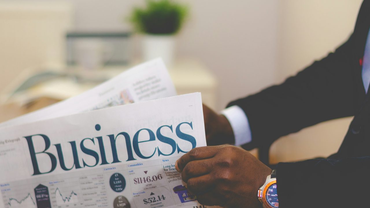 business persons' hands holding a newspaper that reads: business