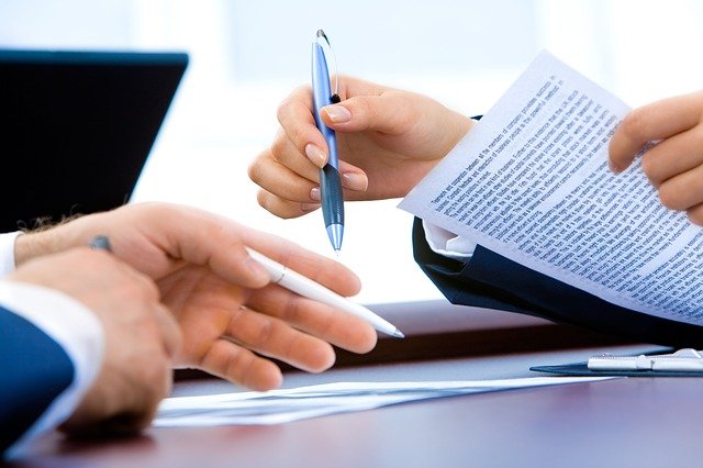 close up of two sets of hands seemingly arguing over a contract with both, using pens, to point to a specific paragraph