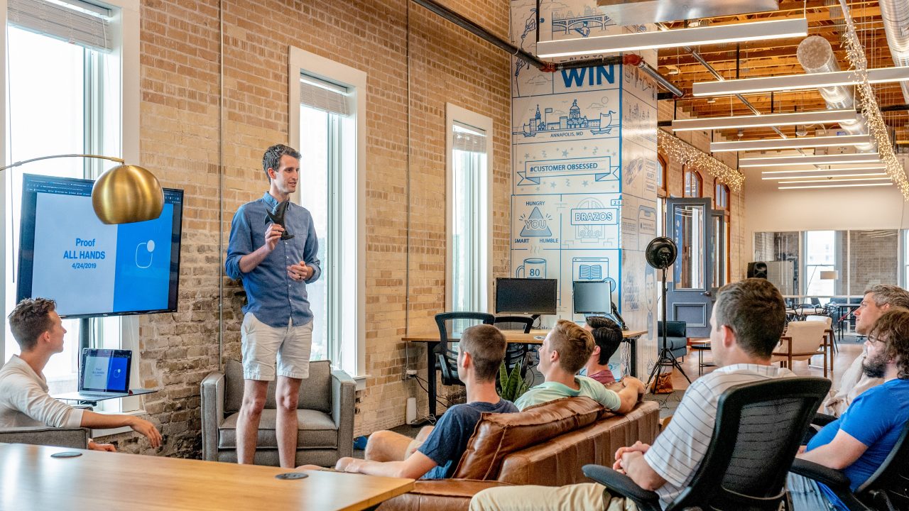 Man at the front of the room presenting a slideshow presentation to his employees