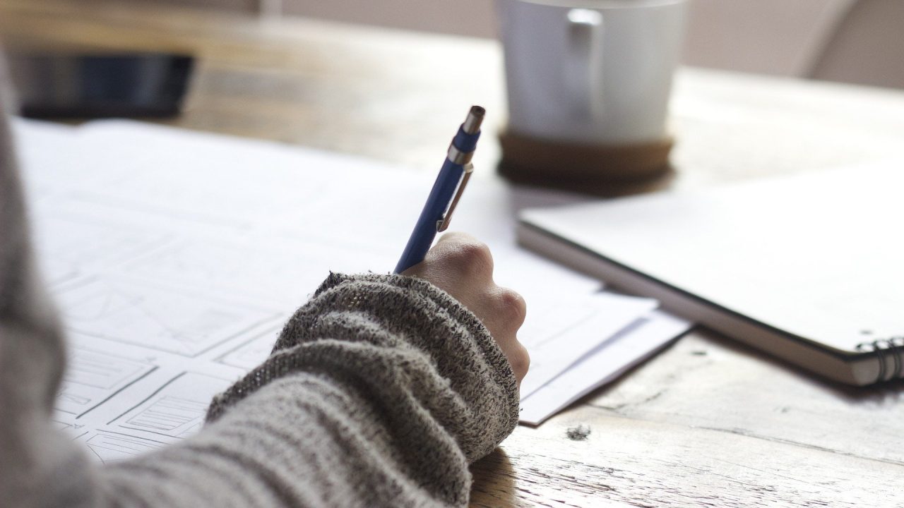 a person's hand filling out a form atop numerous papers.