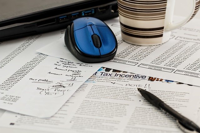 scattered tax forms on a desk with a computer mouse, coffee cup and pen