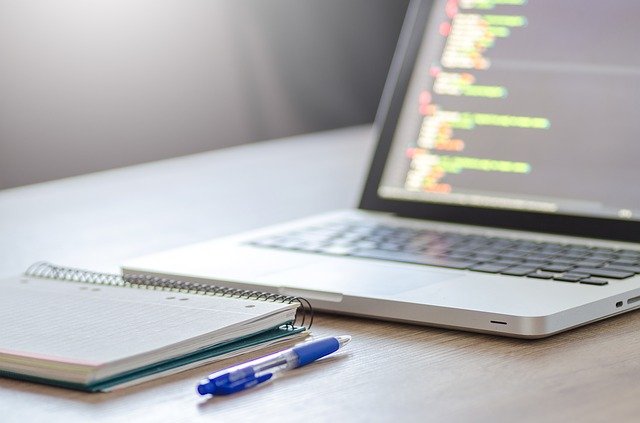 pen and notepad in front of laptop with code on display screen