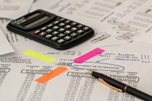 calculator and pen atop a stack of unorganized papers with highlights and circles around the tax implication