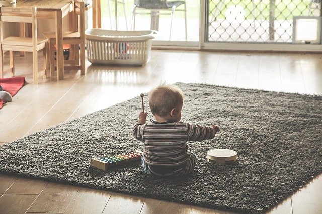 a toddler on a carpet playing a drum and xylophone in an empty house