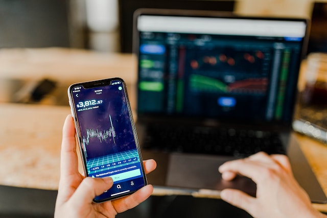 person looking on their phone and laptop tracking the stock market