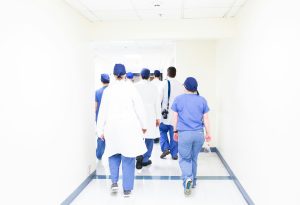 white hospital hallway as doctors and nurses in labcoats and scrubs walk down a cooridor